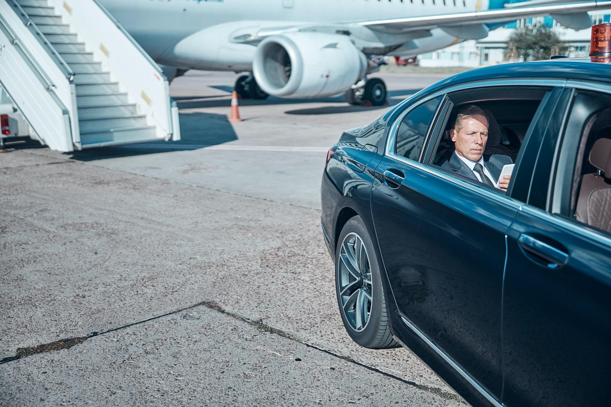 Businessman with smartphone in car at airport